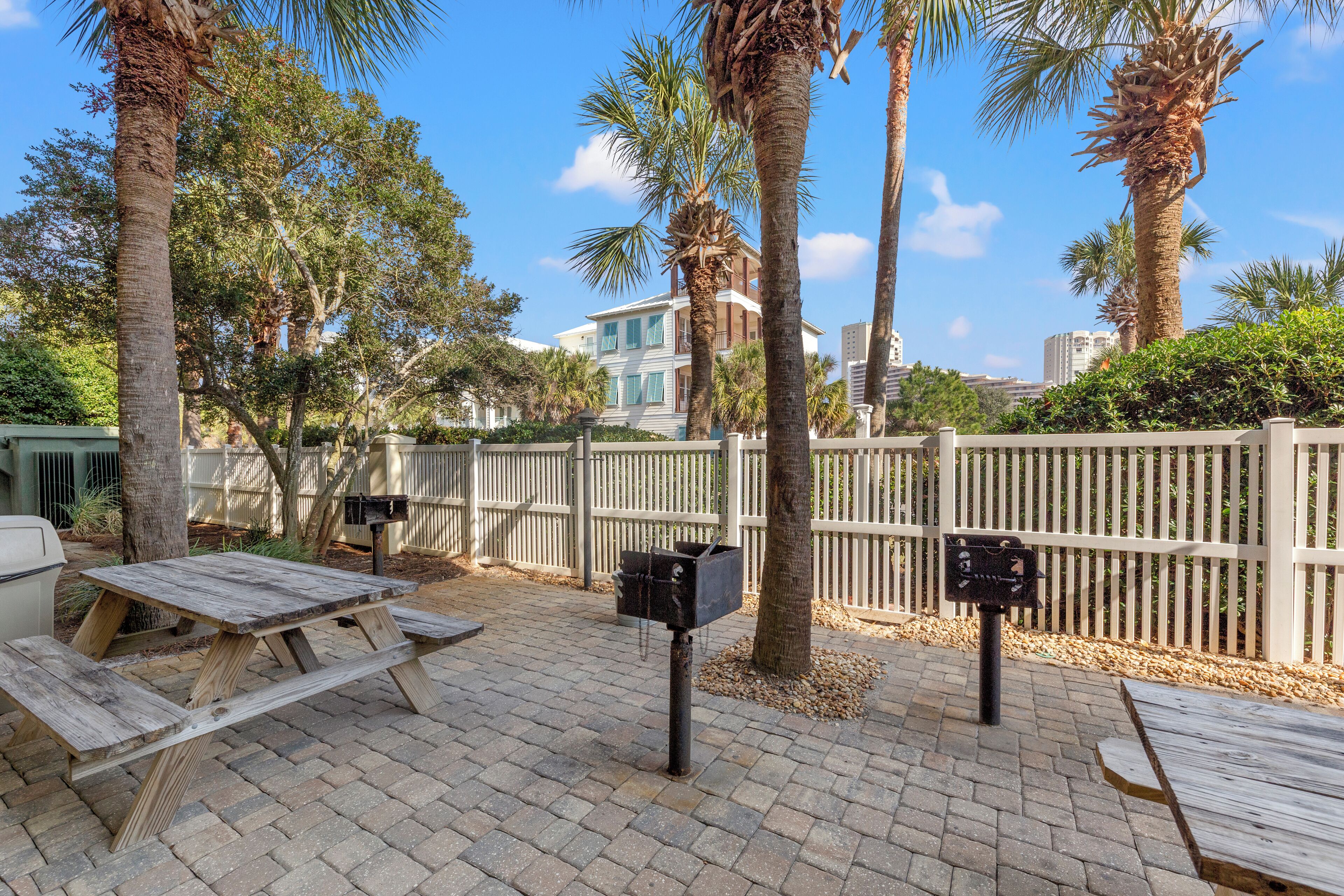 A patio area with picnic tables and mailboxes, surrounded by palm trees and a white fence.