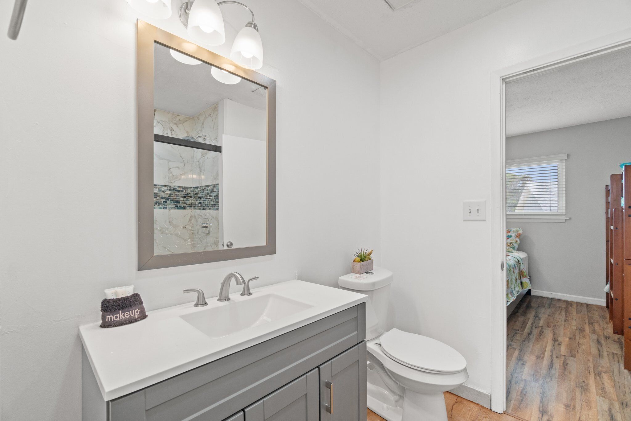 A modern bathroom with a white sink, a mirror with lights, a toilet, and a small plant on the sink.