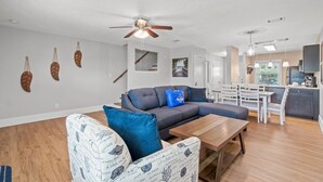 A modern living room with a sectional sofa, a wooden coffee table, and a dining area with a white table and chairs. - 120 Palm Beach Dr A - La Casa Turquesa (Panama City Beach)