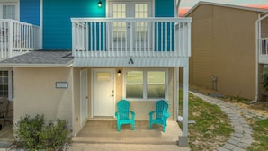 A two-story building with a balcony, a door, and two chairs outside. - 120 Palm Beach Dr A - La Casa Turquesa (Panama City Beach)