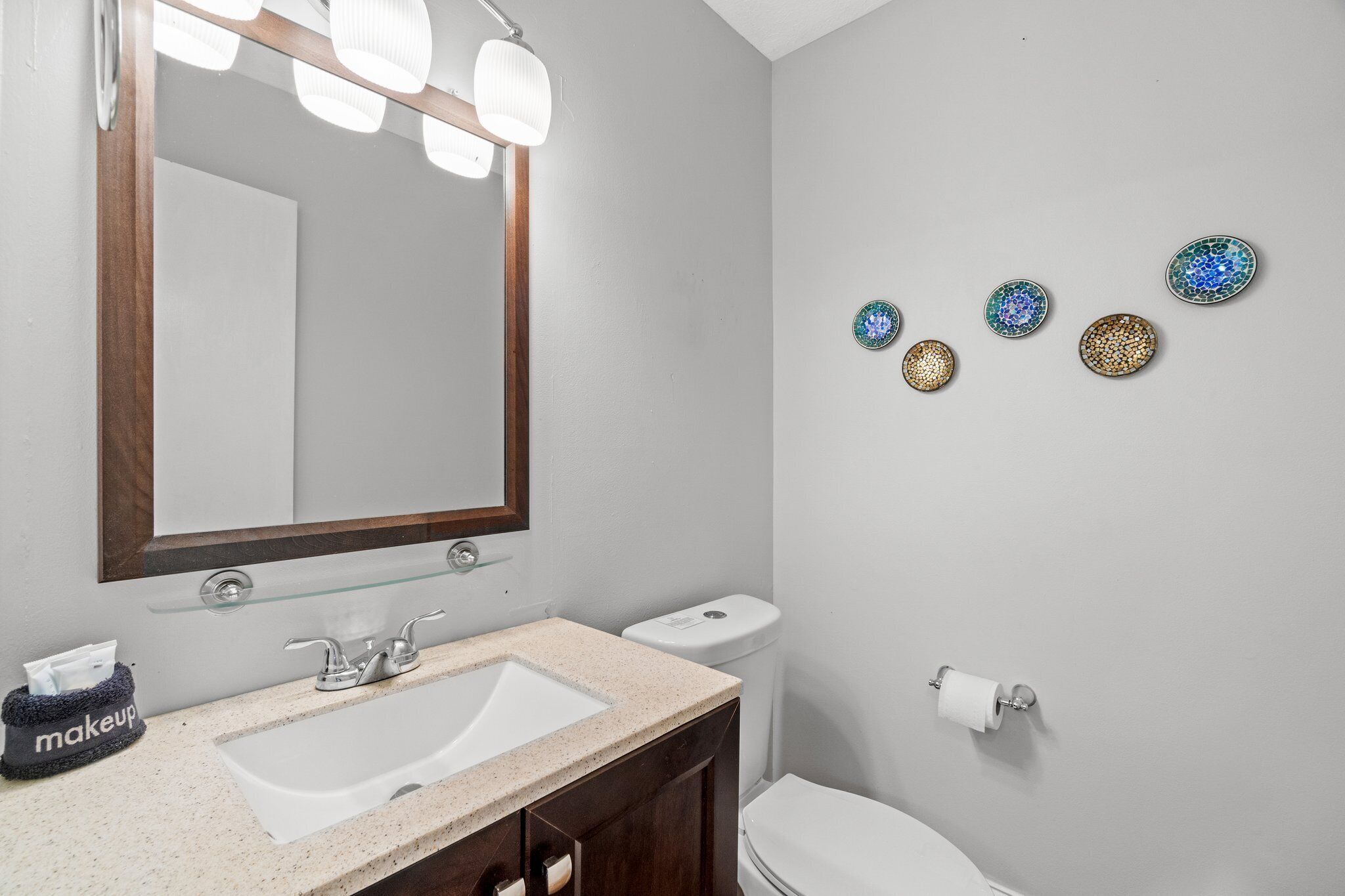 A bathroom with a large mirror, a sink, a toilet, and decorative plates on the wall.