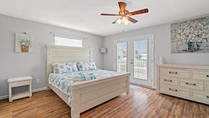 A bedroom with a wooden bed, a ceiling fan, a dresser, and a painting on the wall. - 120 Palm Beach Dr A - La Casa Turquesa (Panama City Beach)