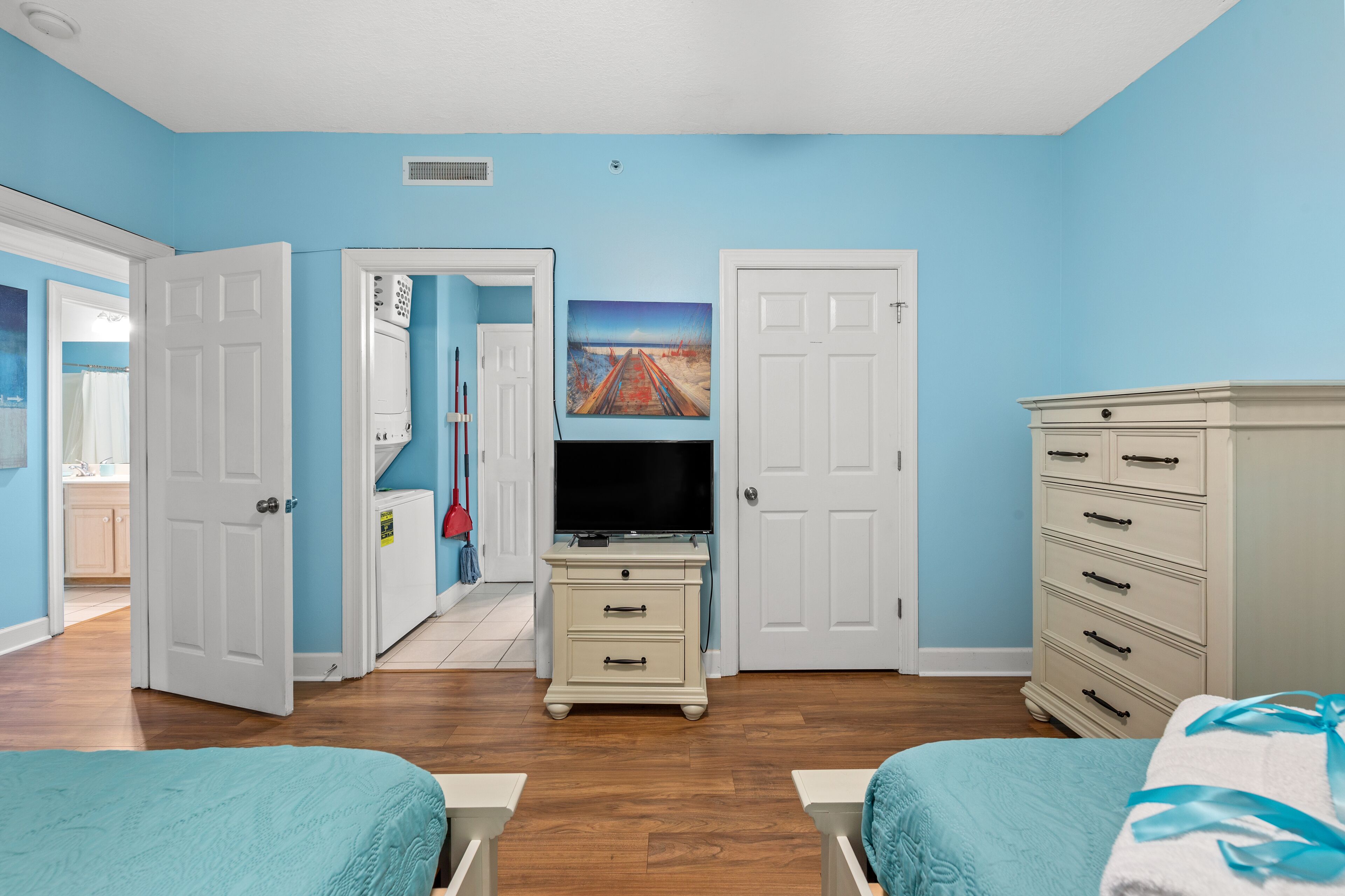 A bedroom with two beds, a dresser, a television, and a painting on the wall.