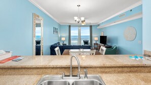 A kitchen with granite countertops, a double sink, and a view of the ocean through large windows. - Large Balcony! Gulf Front Master Suite! Many Amenities On-site! (Panama City Beach)