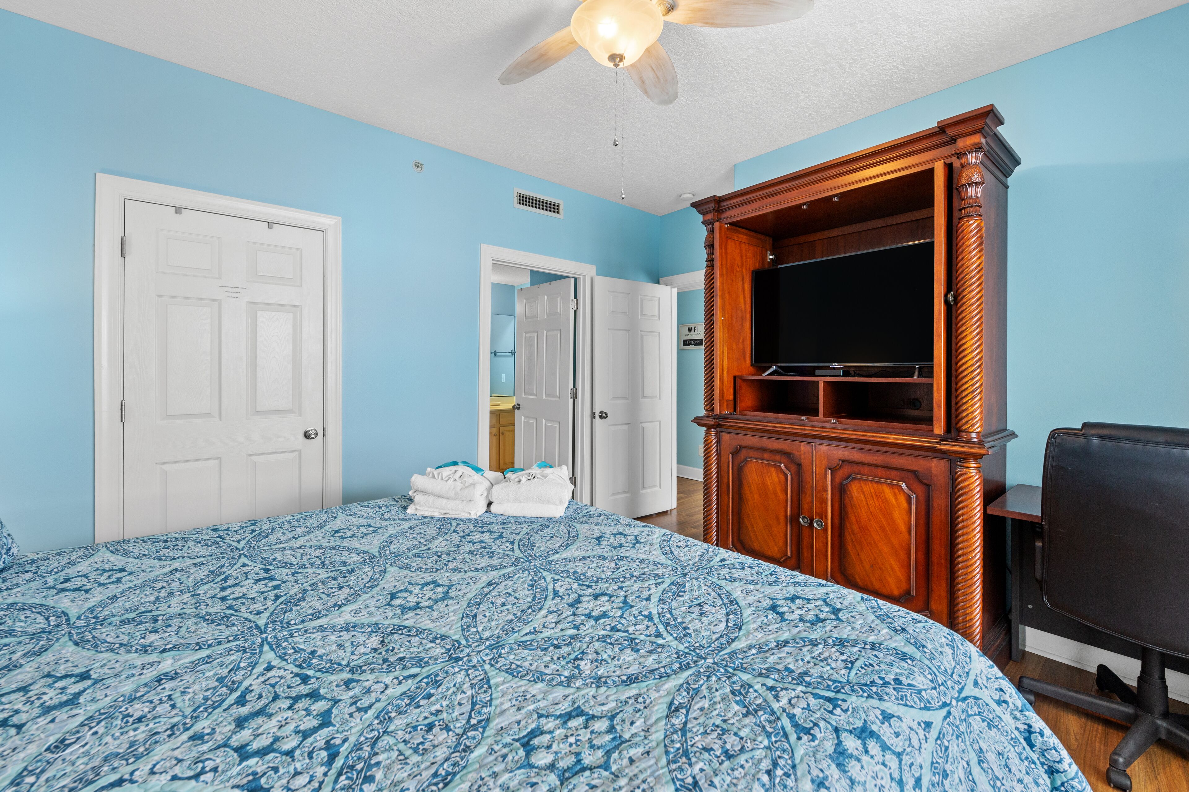 A bedroom with a large bed, a wooden cabinet with a television, and a ceiling fan.