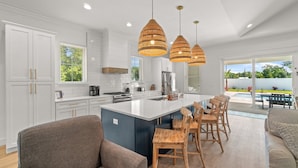 Een moderne keuken met witte kasten, een groot eiland en hangende lampen.