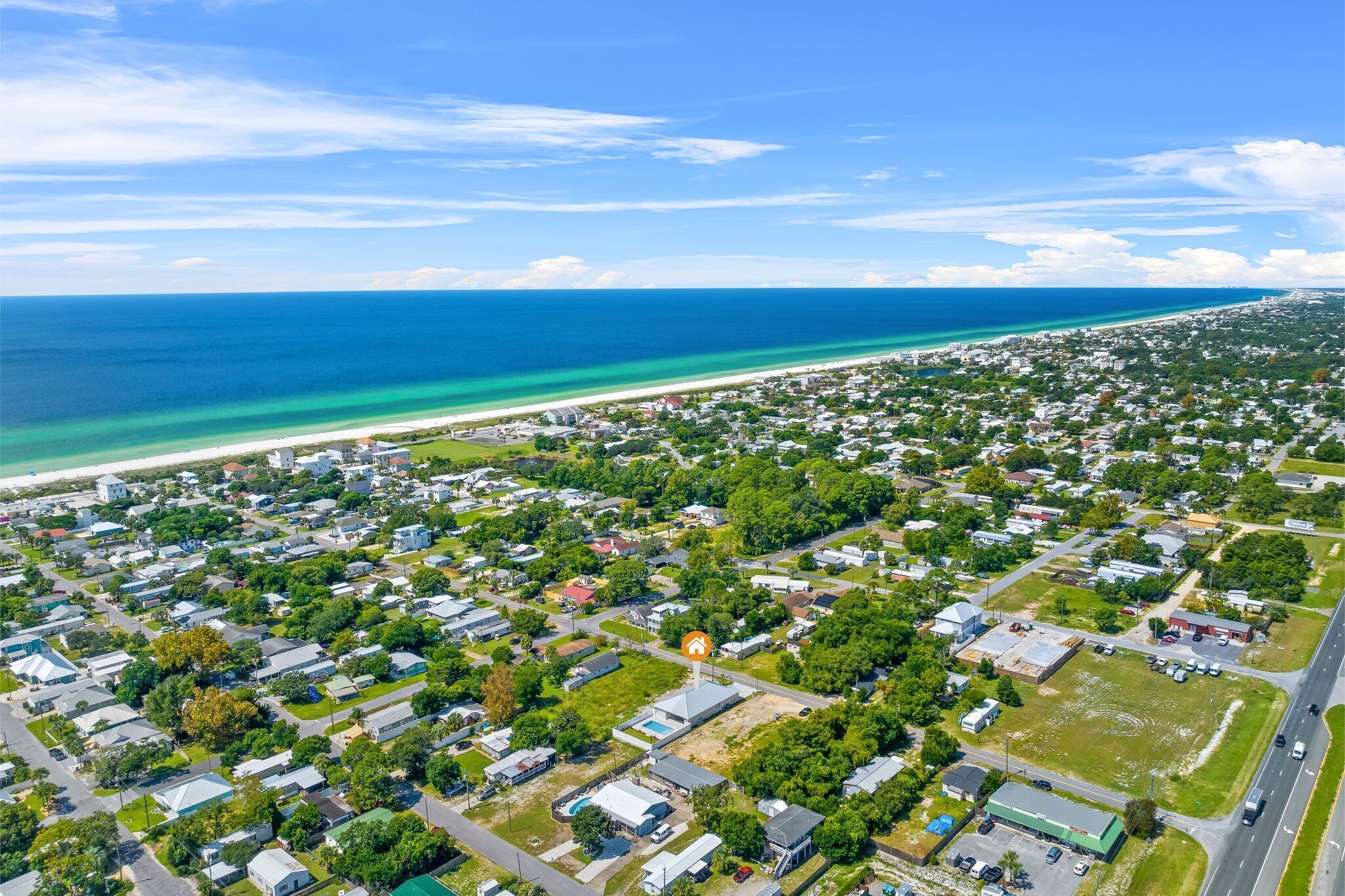 An aerial view of a coastal residential area with houses, roads, and a beach.