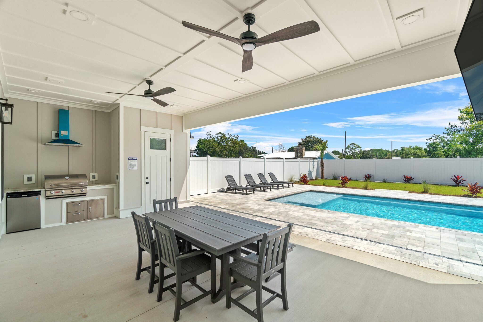 An outdoor patio with a pool, a dining table with chairs, a grill, and a ceiling fan.