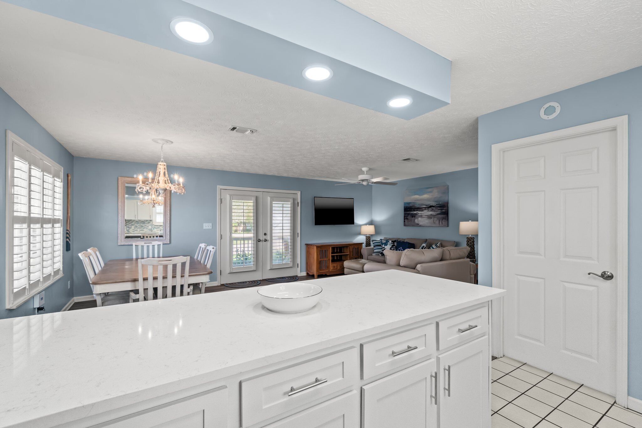 A modern kitchen with white cabinetry, a large island, and a dining area with a chandelier.