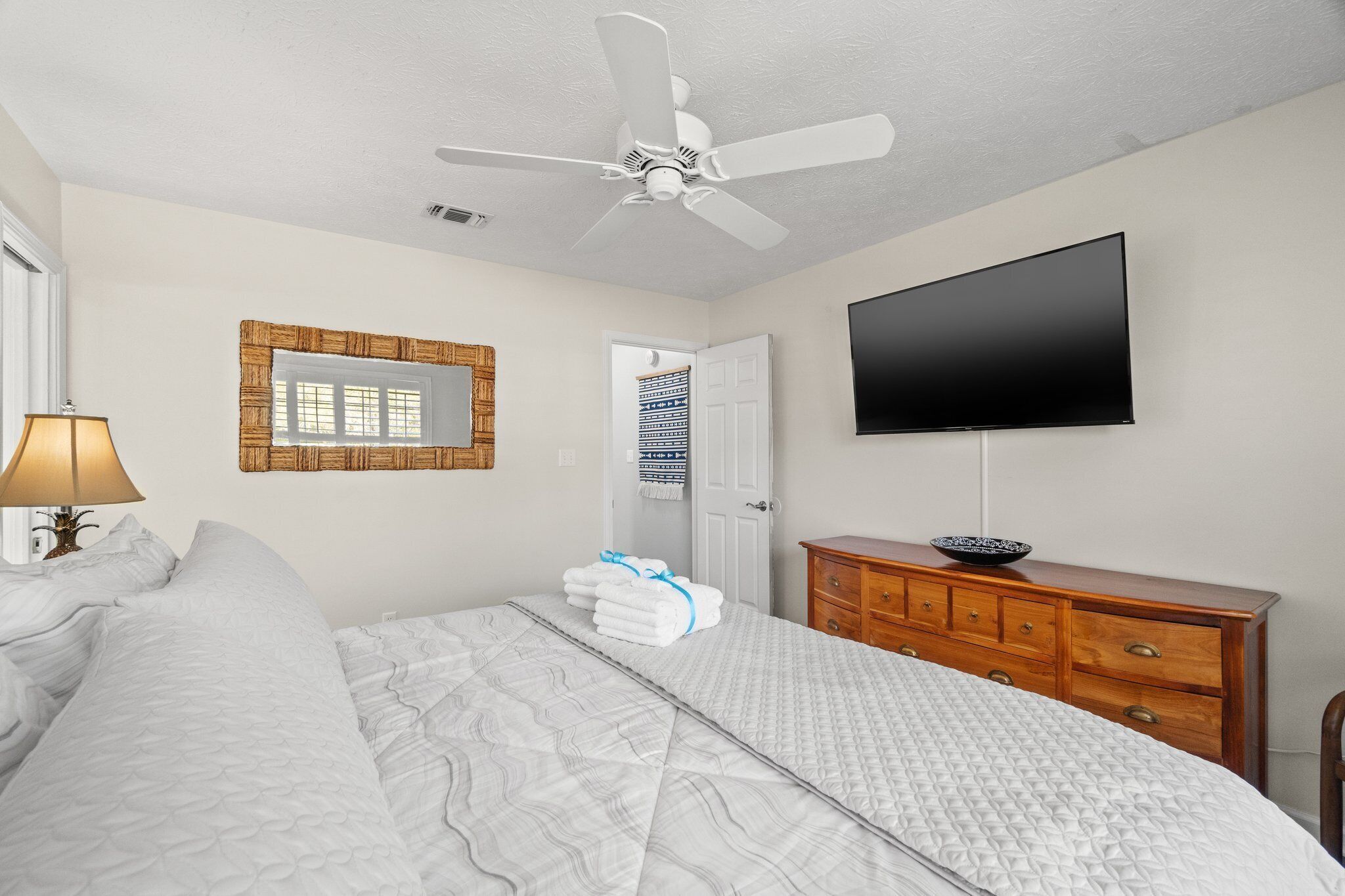 A bedroom with a bed, a dresser, a television, and a ceiling fan.