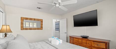 A bedroom with a bed, a dresser, a television, and a ceiling fan.