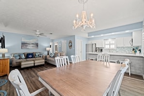A spacious living room with a large wooden dining table, a beige sofa, and a chandelier. - Contemporary Bungalow / West End PCB / Available Now! / Perfect for Family (Panama City Beach)