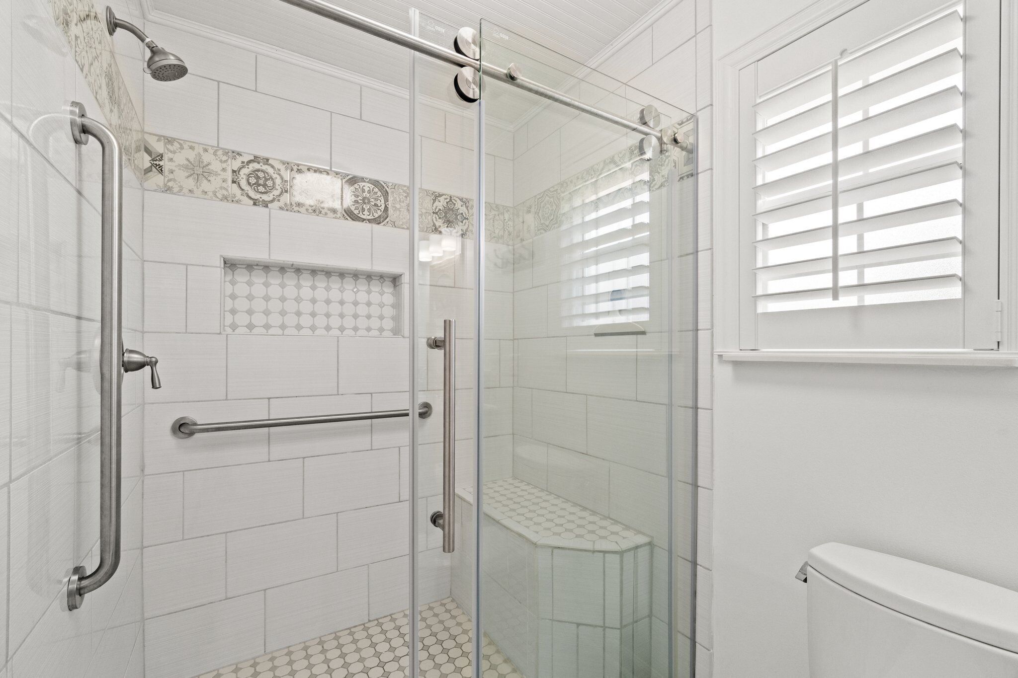 Une salle de bain moderne avec une douche à parois de verre, des murs recouverts de carreaux blancs et des toilettes.