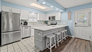 Una cocina moderna con armarios blancos, una isla grande con taburetes, electrodomésticos de acero inoxidable y una pared de acento azul.