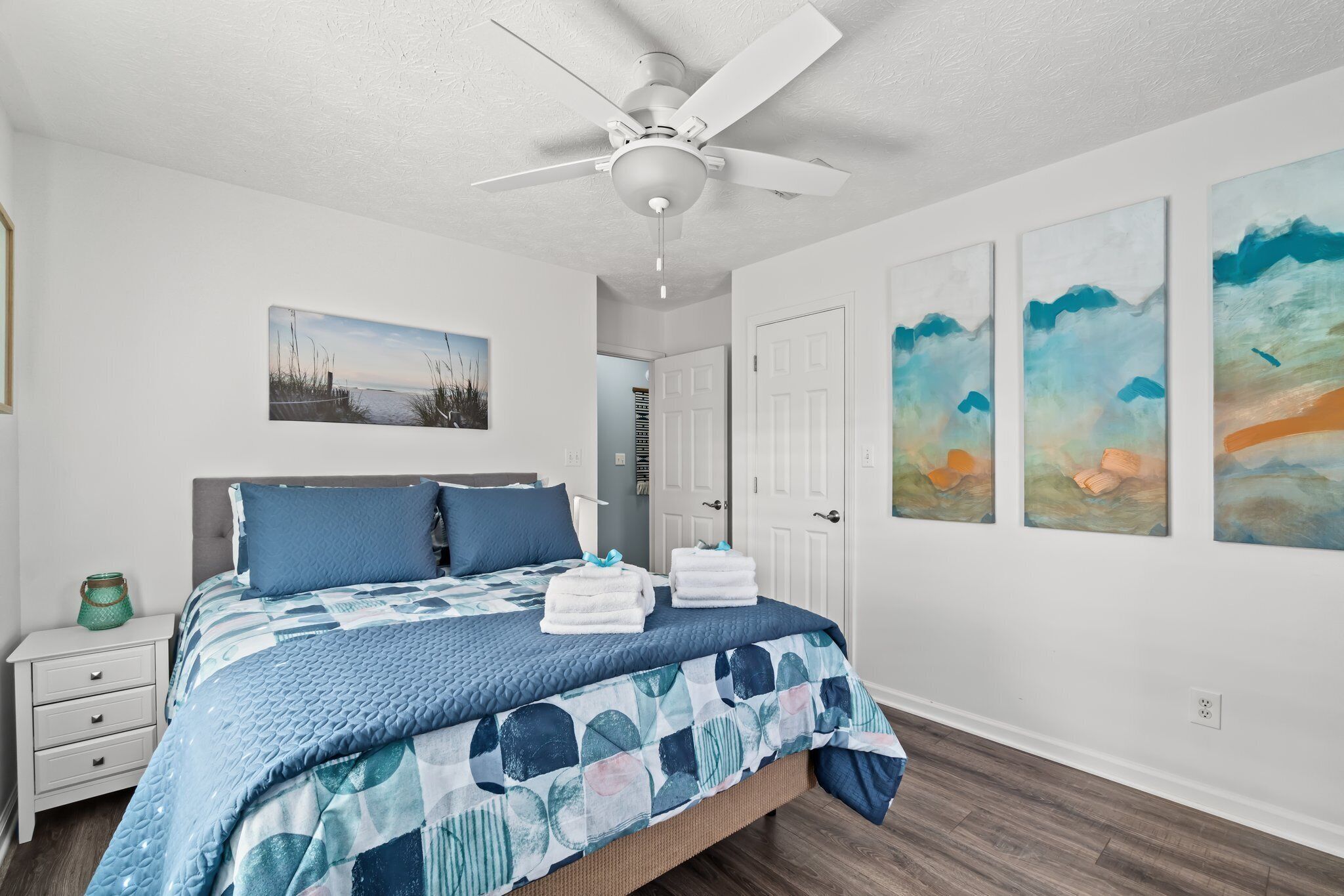 A bedroom with a bed, a nightstand, a ceiling fan, and wall art.