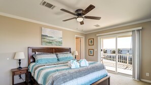 A bedroom with a large bed, a ceiling fan, a nightstand, a painting, and a view of the outside through a sliding glass door. - Summer Dayz - Families Love It Here, Just Across From the Beach (Panama City Beach)