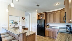 A kitchen with granite countertops, wooden cabinets, a black refrigerator, and a built-in island with bar stools. - Summer Dayz - Families Love It Here, Just Across From the Beach (Panama City Beach)