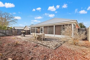 Ein Haus mit überdachter Terrasse, Grill und umzäuntem Garten.