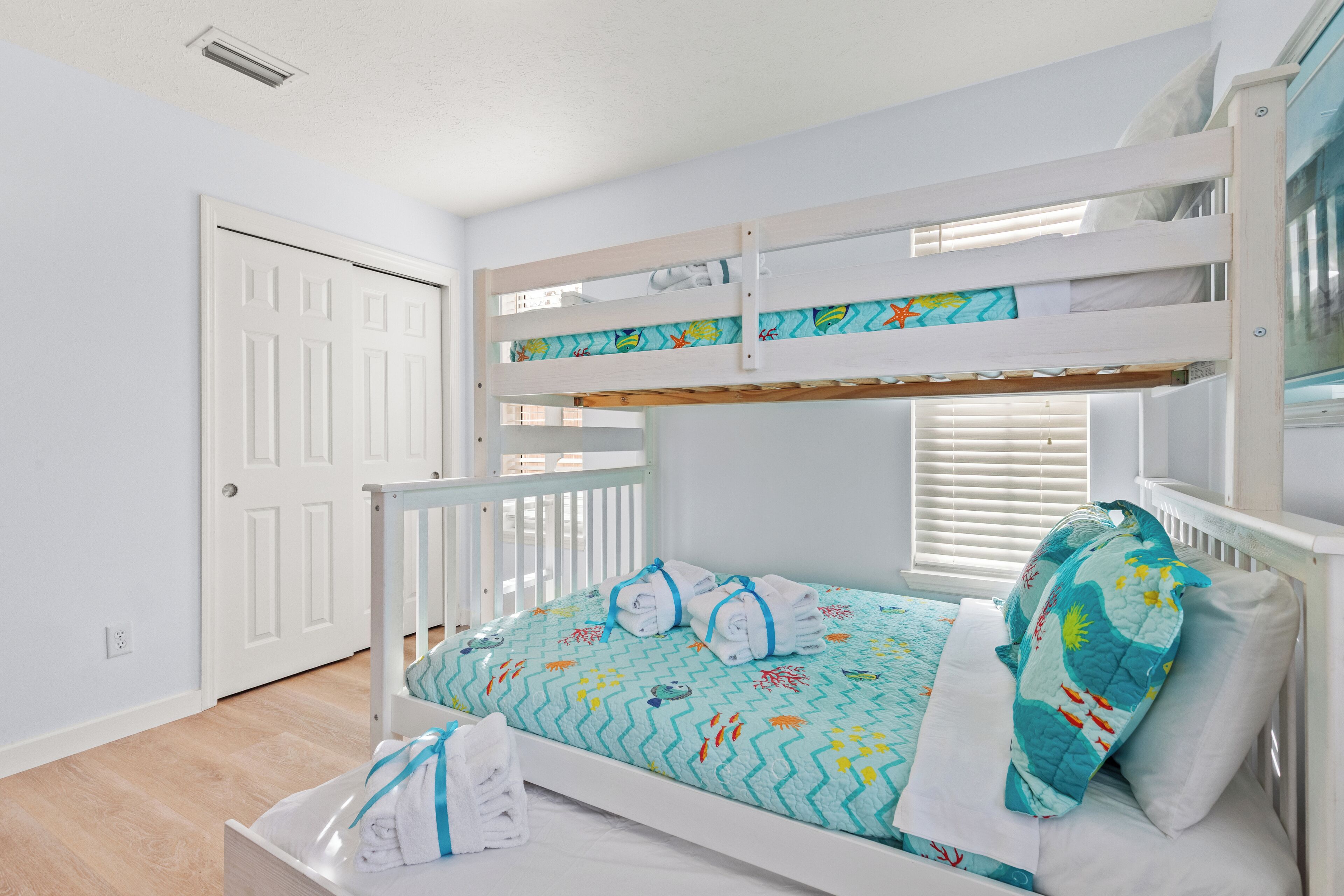 A bunk bed with a patterned bedspread, a white door, and a window with blinds.