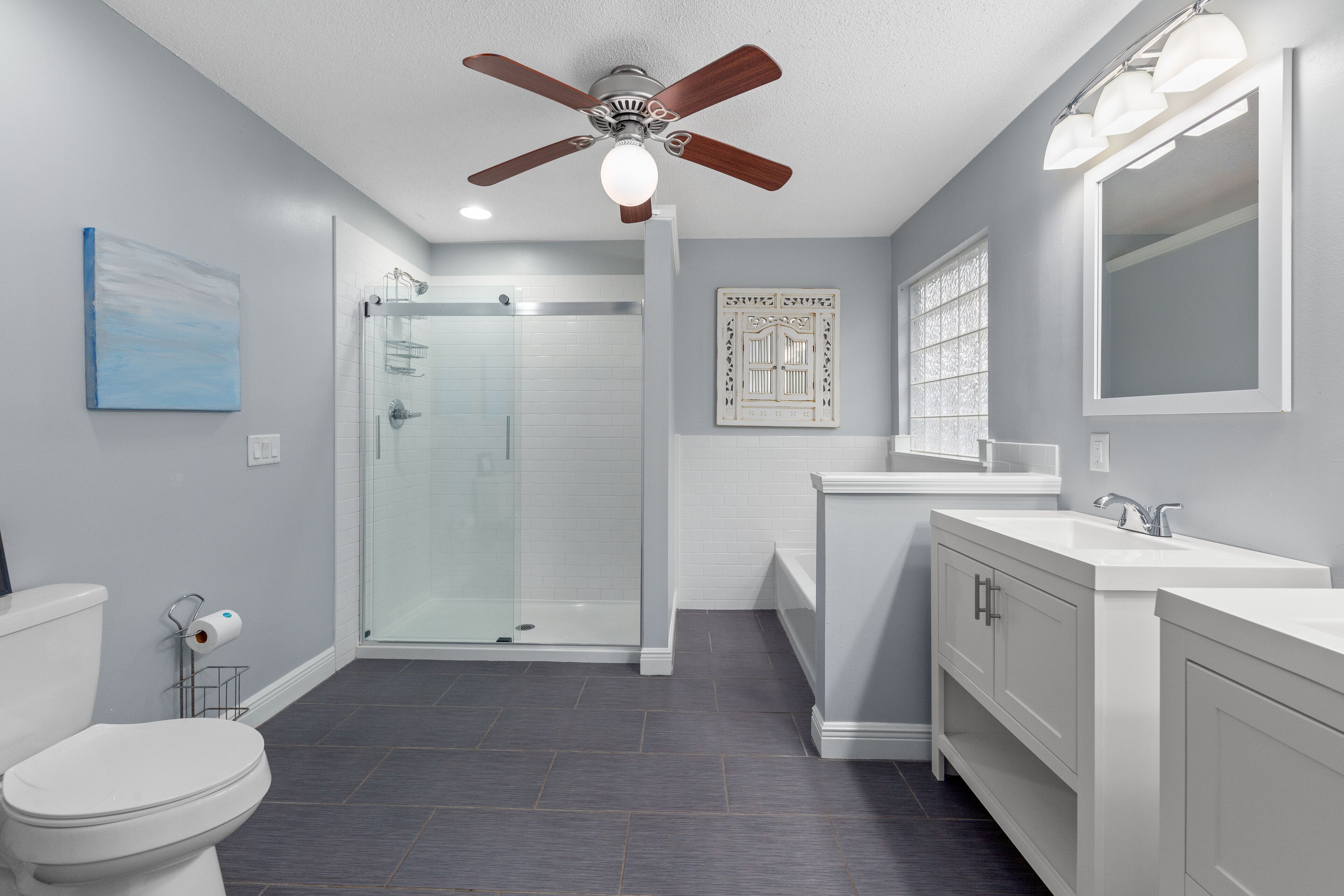 A modern bathroom with a shower, toilet, vanity, and ceiling fan.