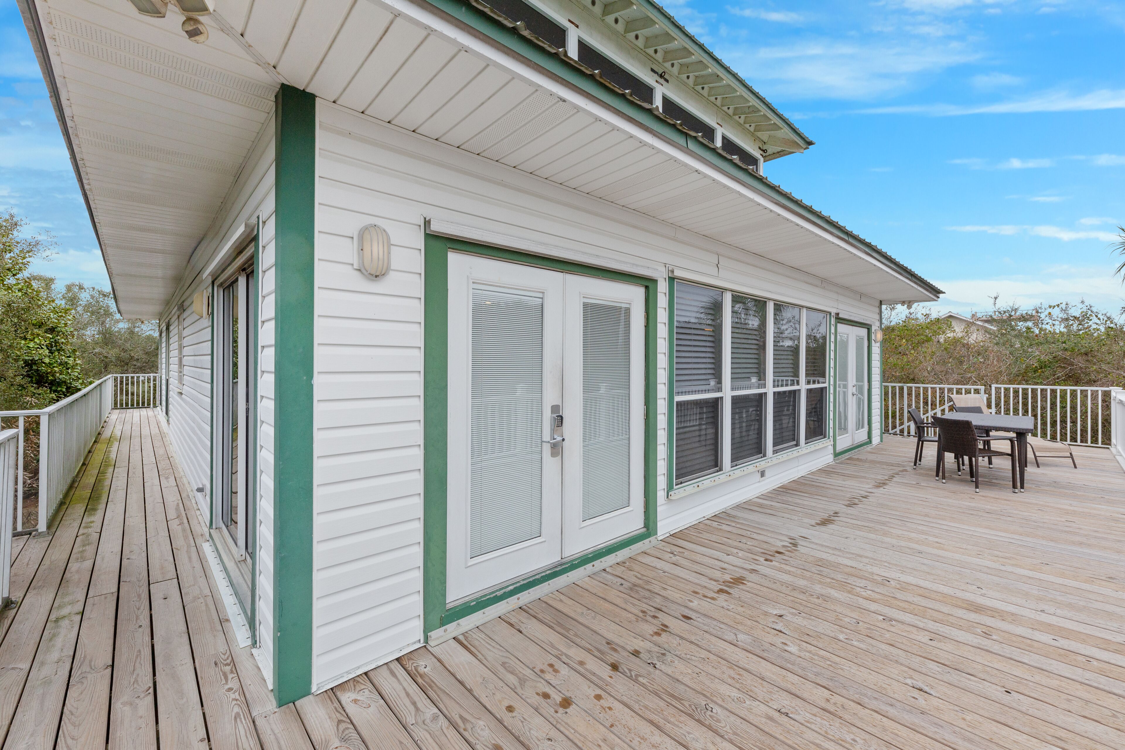 A wooden deck with a white building featuring a green trim and a sliding glass door.