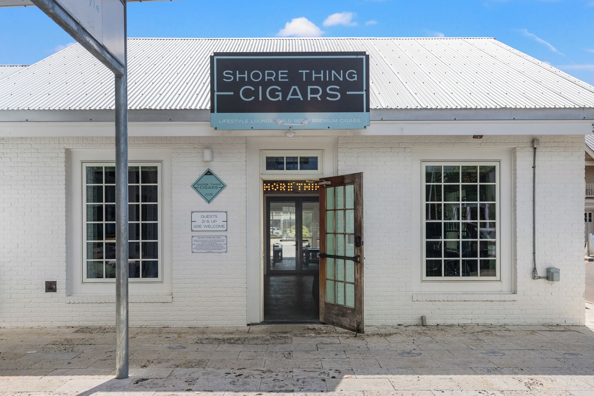A white building with a sign reading "Shore Thing Cigars" and a sign indicating "Guests 216 Up".