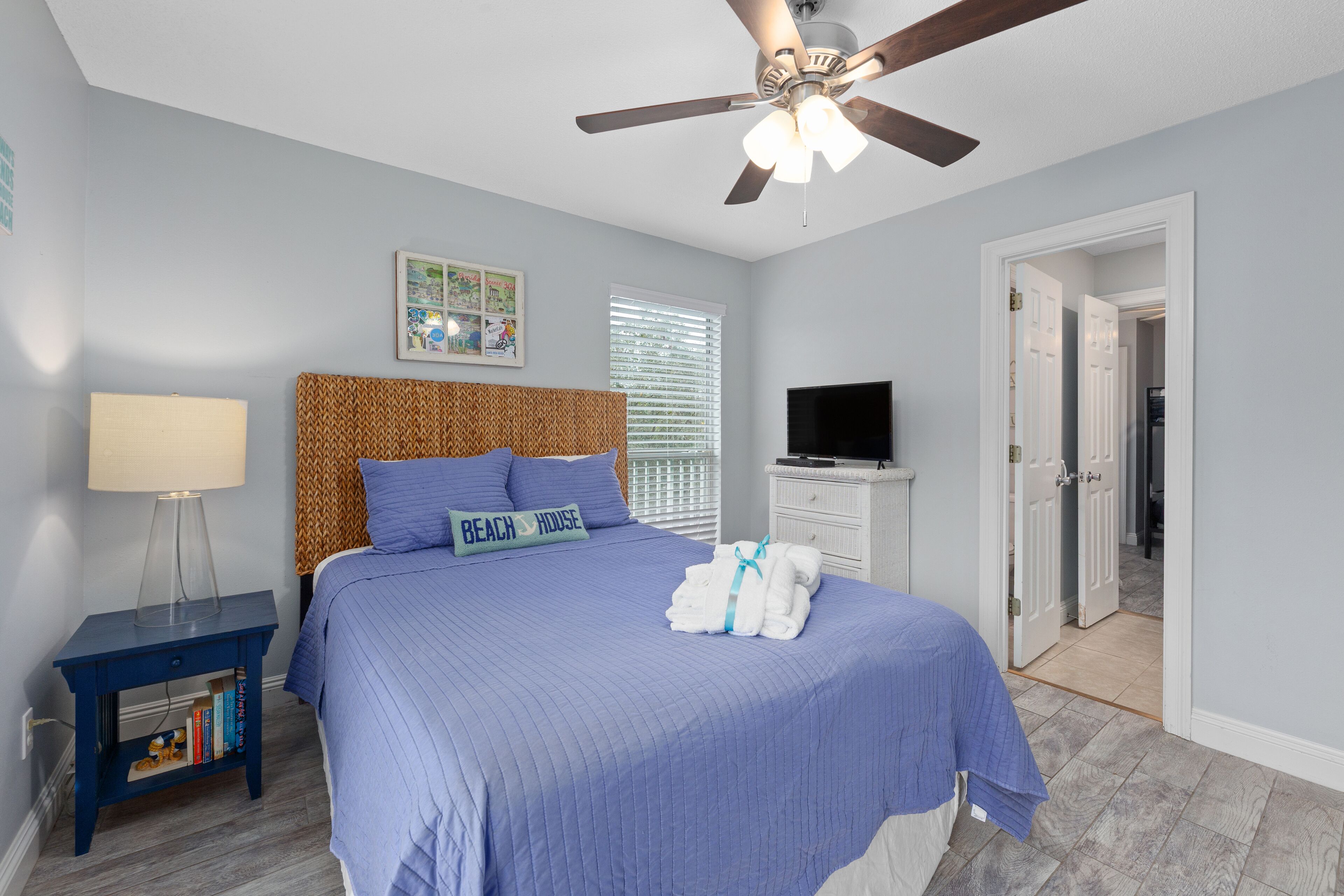 A bedroom with a bed, a ceiling fan, a TV, and a door leading to another room.