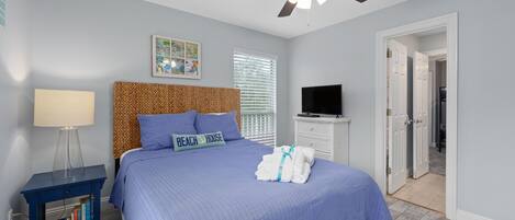 A bedroom with a bed, a ceiling fan, a TV, and a door leading to another room.