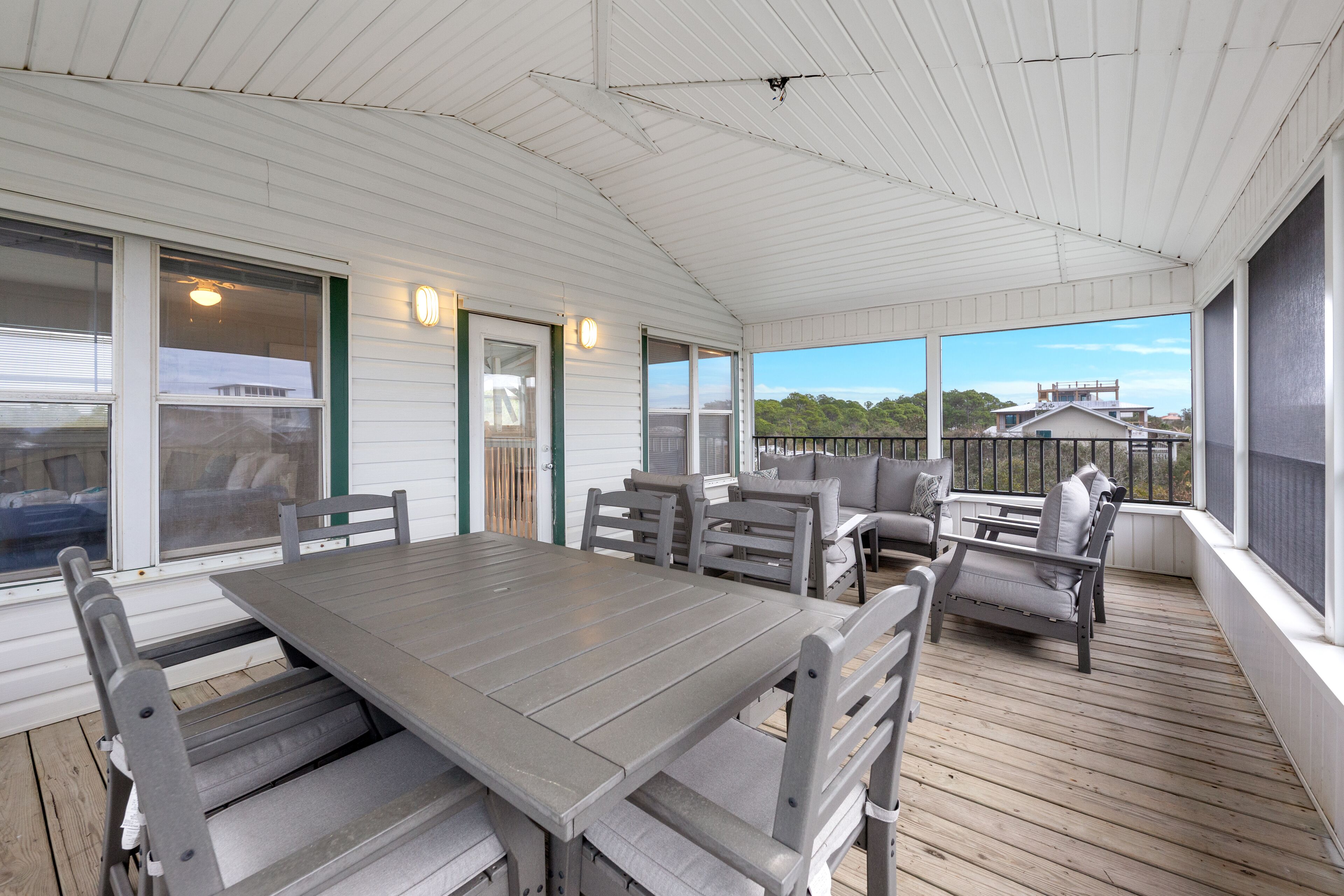 A covered outdoor patio with a wooden table and chairs, a sofa, and a view of the surrounding area.