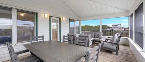 A covered outdoor patio with a wooden table and chairs, a sofa, and a view of the surrounding area.