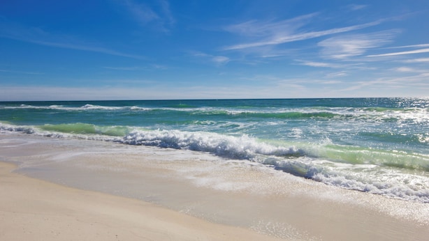 Ein Strand mit ankommenden Wellen unter blauem Himmel.