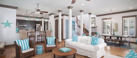 A spacious living room with a white sofa, wicker chairs, a wooden coffee table, and a ceiling fan.