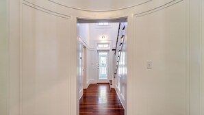 A hallway with a wooden floor, white walls, and a door at the end. - A Seaside Beauty! Book Now - Lot of Outdoor Living Space (Santa Rosa Beach)