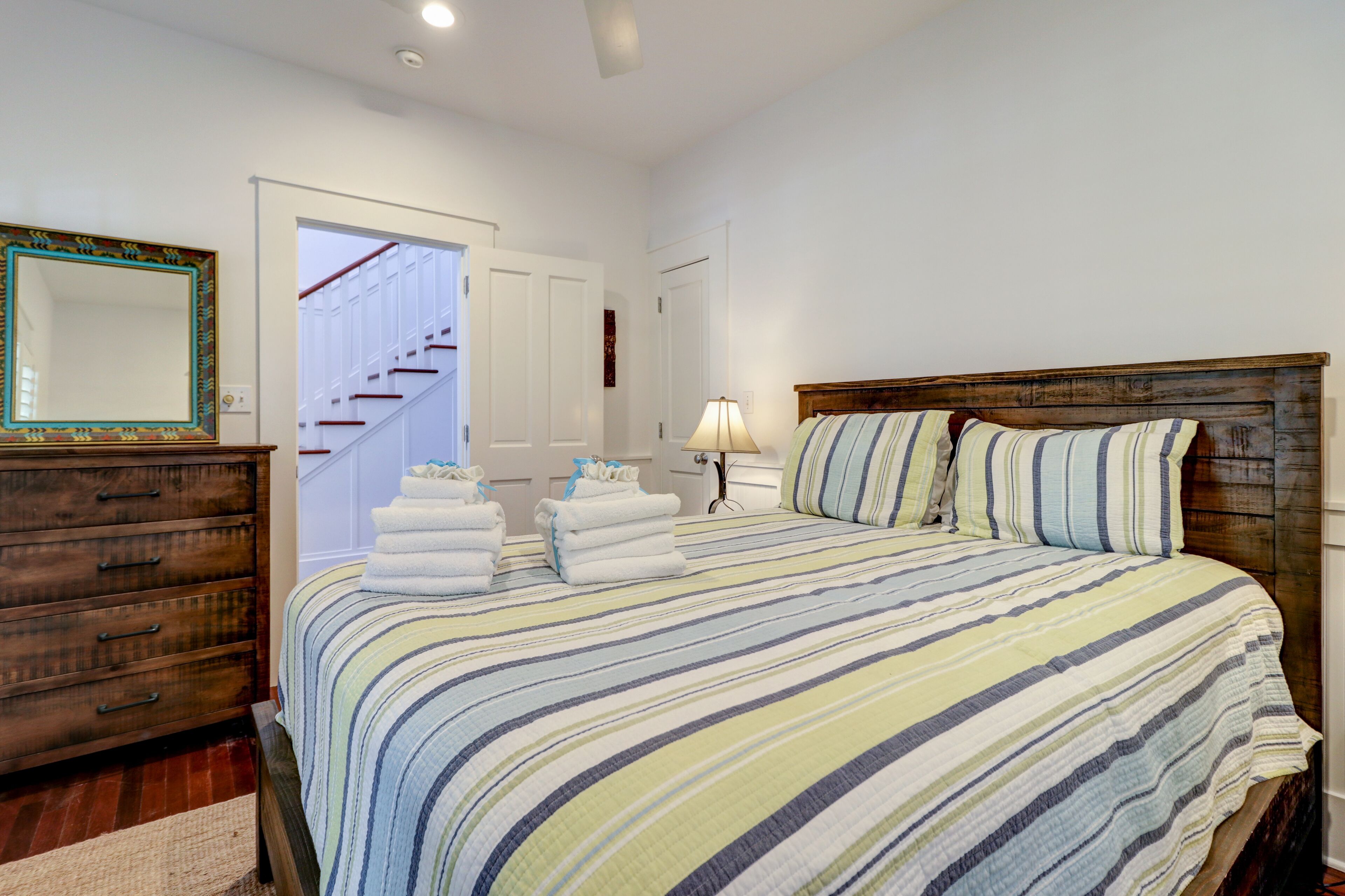 A bedroom with a wooden bed, striped bedding, a dresser, and a mirror.