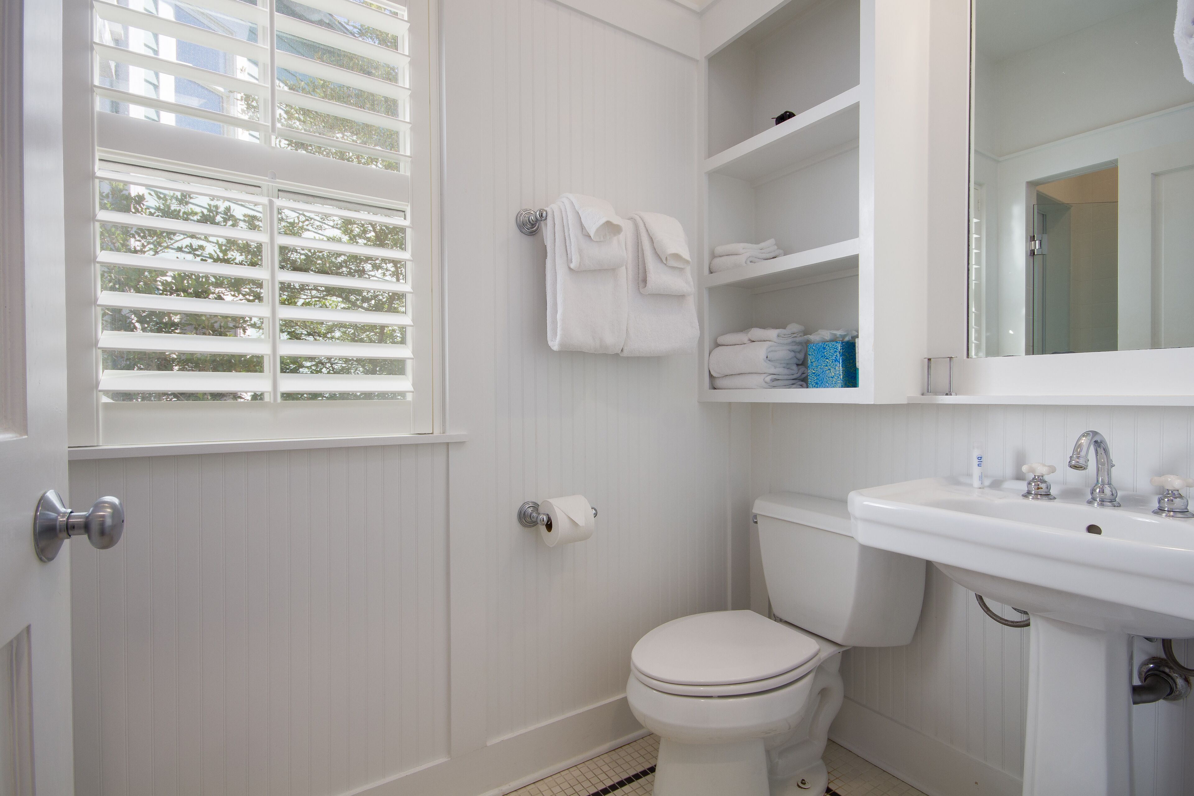 A bathroom with a toilet, a sink, and a window with blinds.