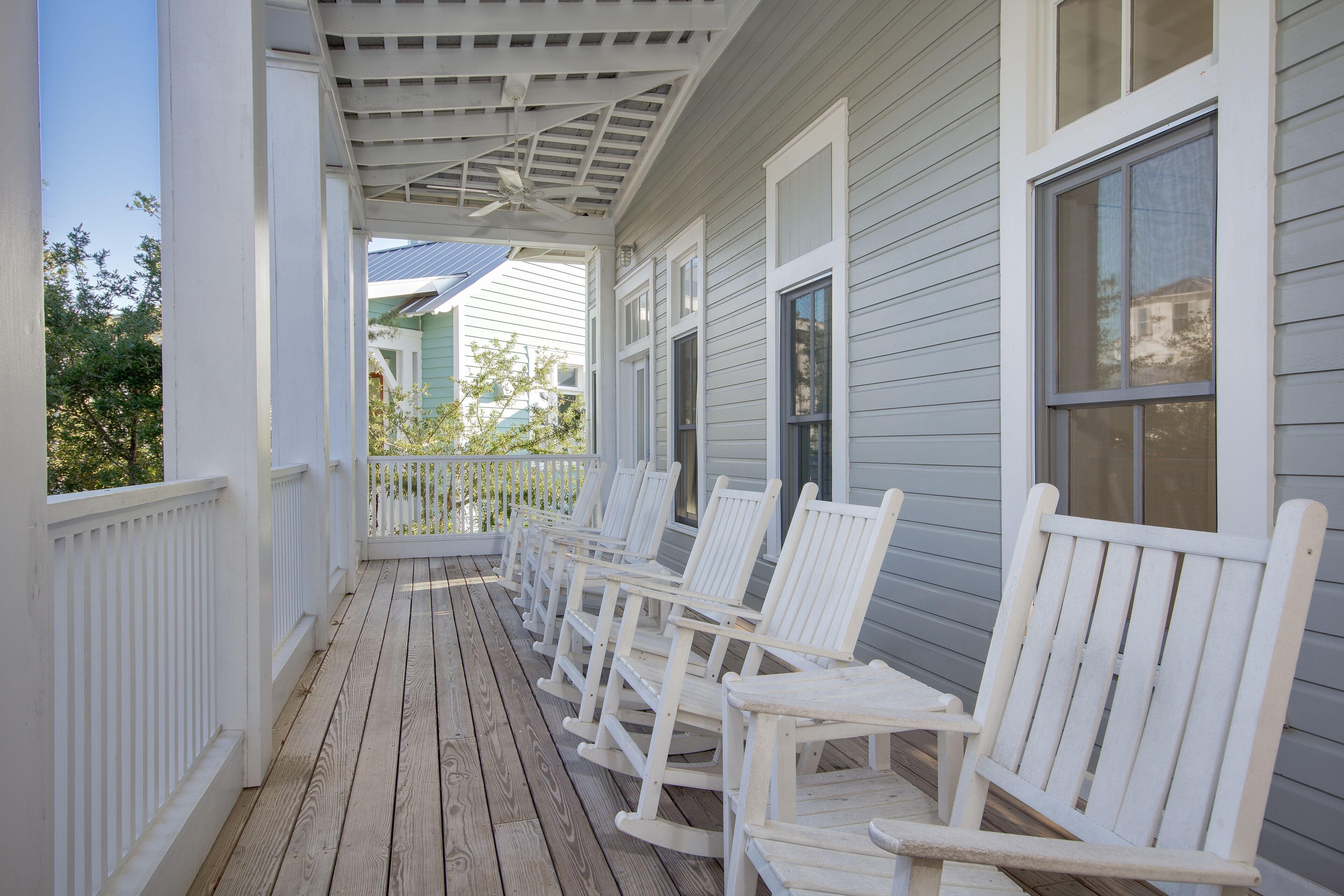 A covered porch with white rocking chairs and a ceiling fan.