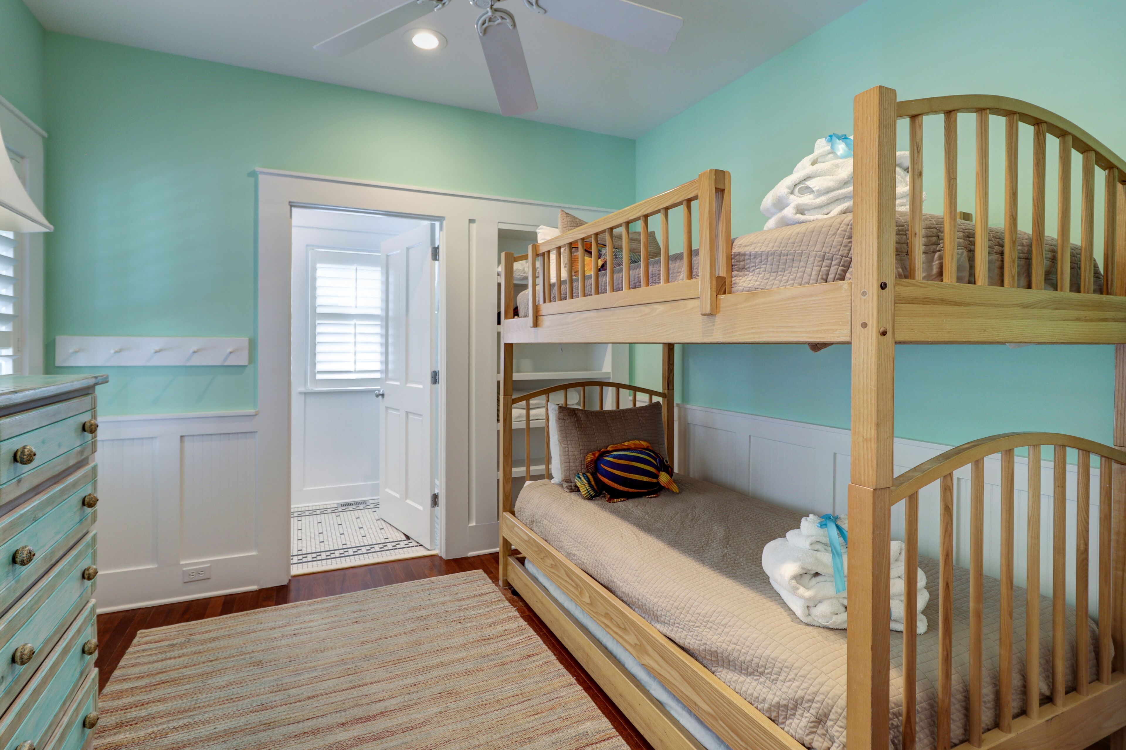 Quarto com beliche, porta que dá para outro aposento, cômoda e ventilador de teto.