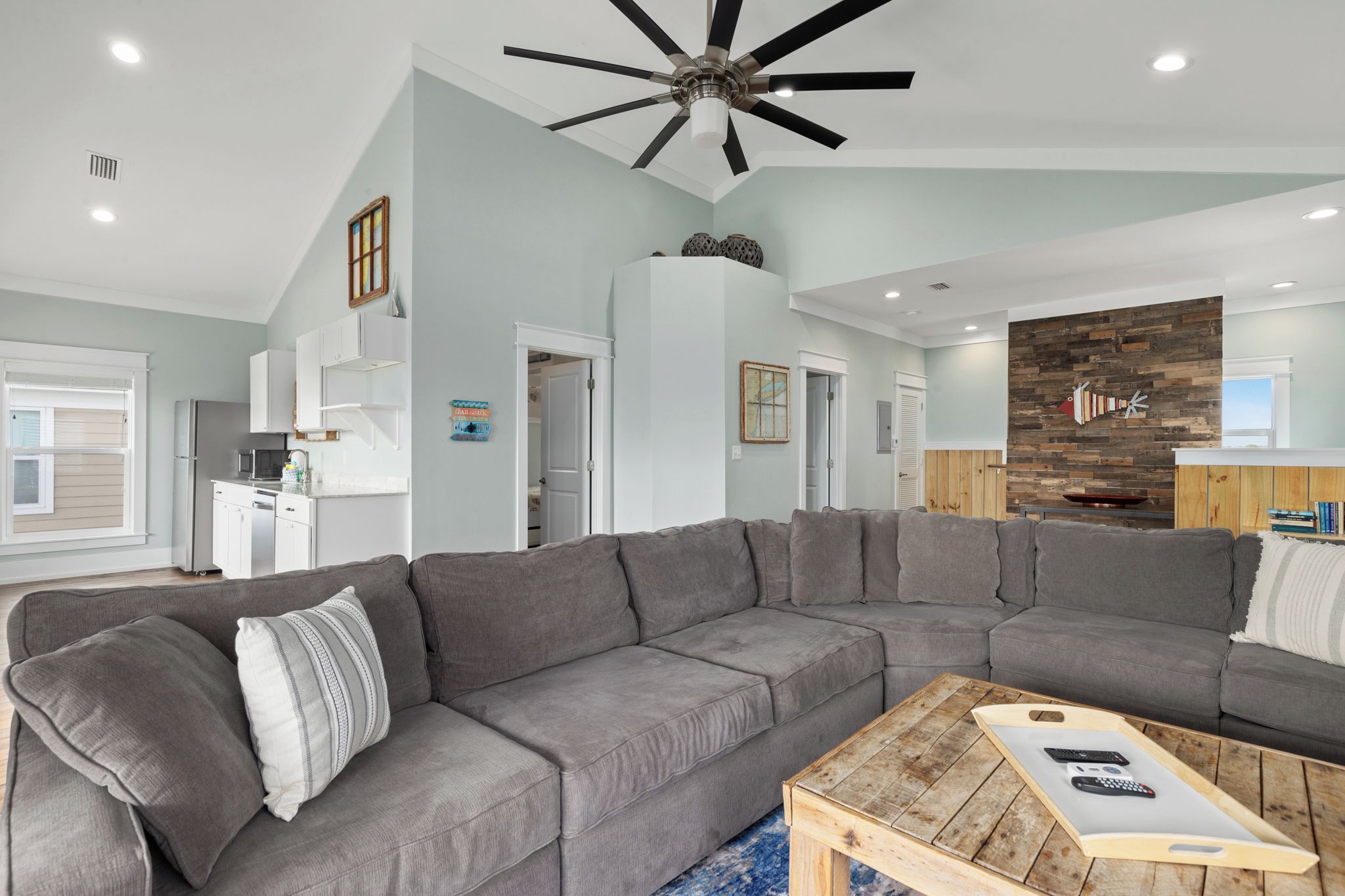 Un salon moderne avec un canapé d’angle, une table basse en bois et un ventilateur de plafond.