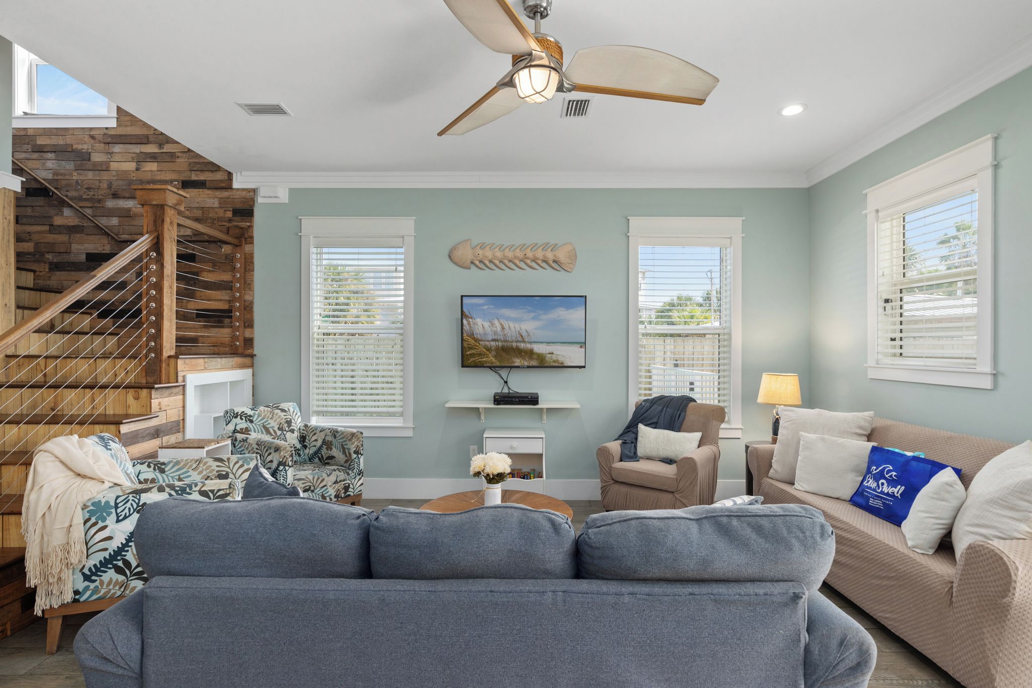 A living room with a staircase, a ceiling fan, a TV, and a fish skeleton decoration.