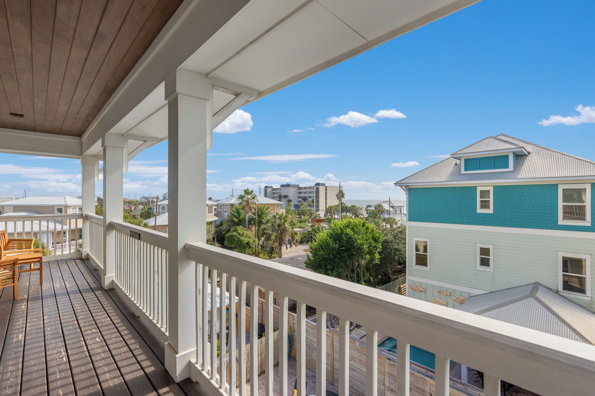 A wooden deck with white railings, overlooking a residential area with houses and greenery.