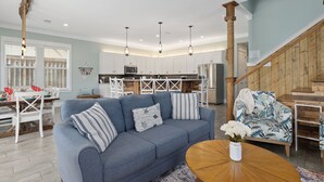 A modern living room with a blue sofa, a wooden coffee table, and a dining area with white chairs and a wooden table.