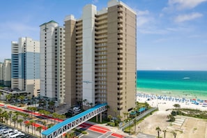 Hotel alto com várias varandas, vista para a praia e área de estacionamento com uma passarela.