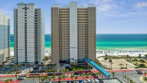 A hotel with a central tower, a beach view, and a parking area with palm trees. - Luxurious Ocean Villa Resort - Gulf Front Paradise With Views! (Panama City Beach)