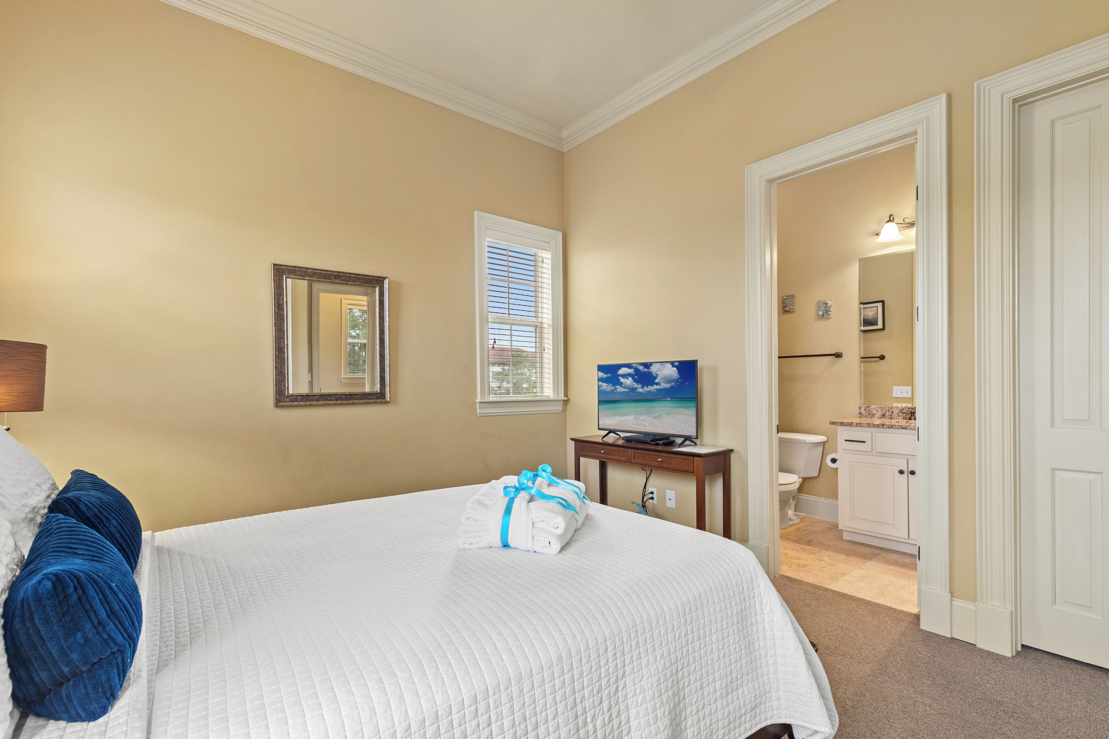 A hotel room with a bed, a television, a bathroom visible through an open door, and a window with blinds.