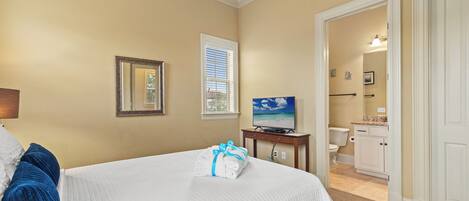 A hotel room with a bed, a television, a bathroom visible through an open door, and a window with blinds.