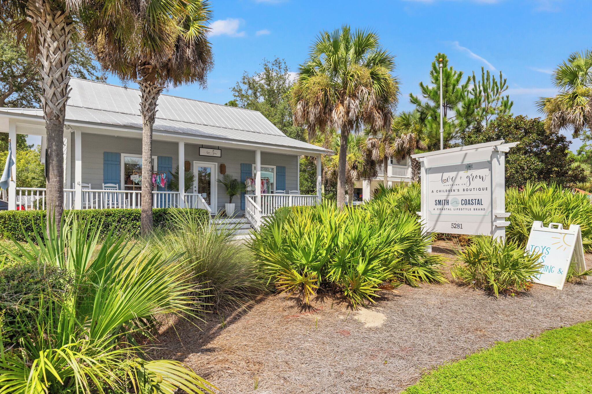 A coastal building with a porch, surrounded by tropical plants and palm trees.
