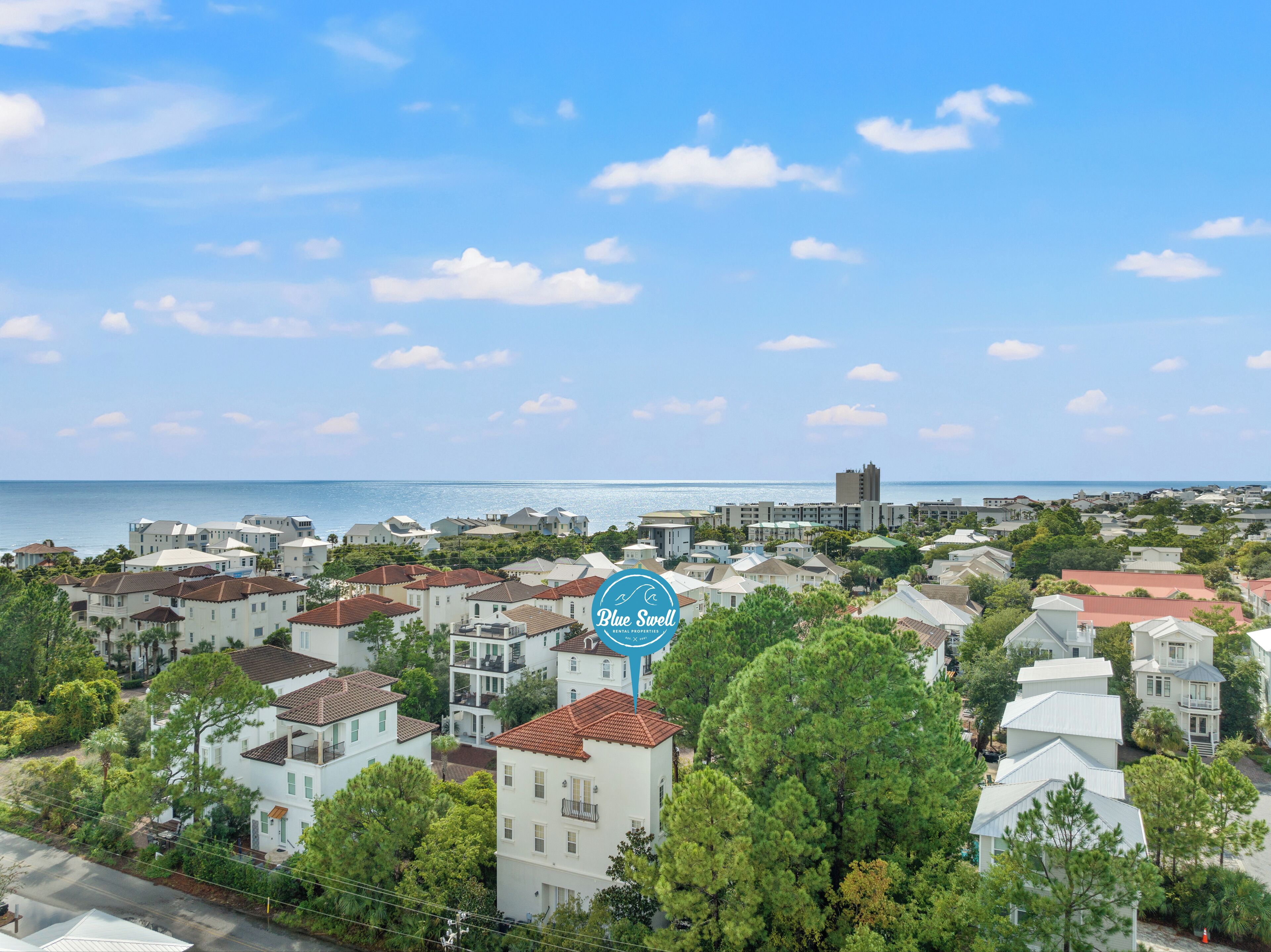 A coastal residential area with a mix of single and multi-story houses, a clear view of the sea, and a prominent Blue Swell logo.