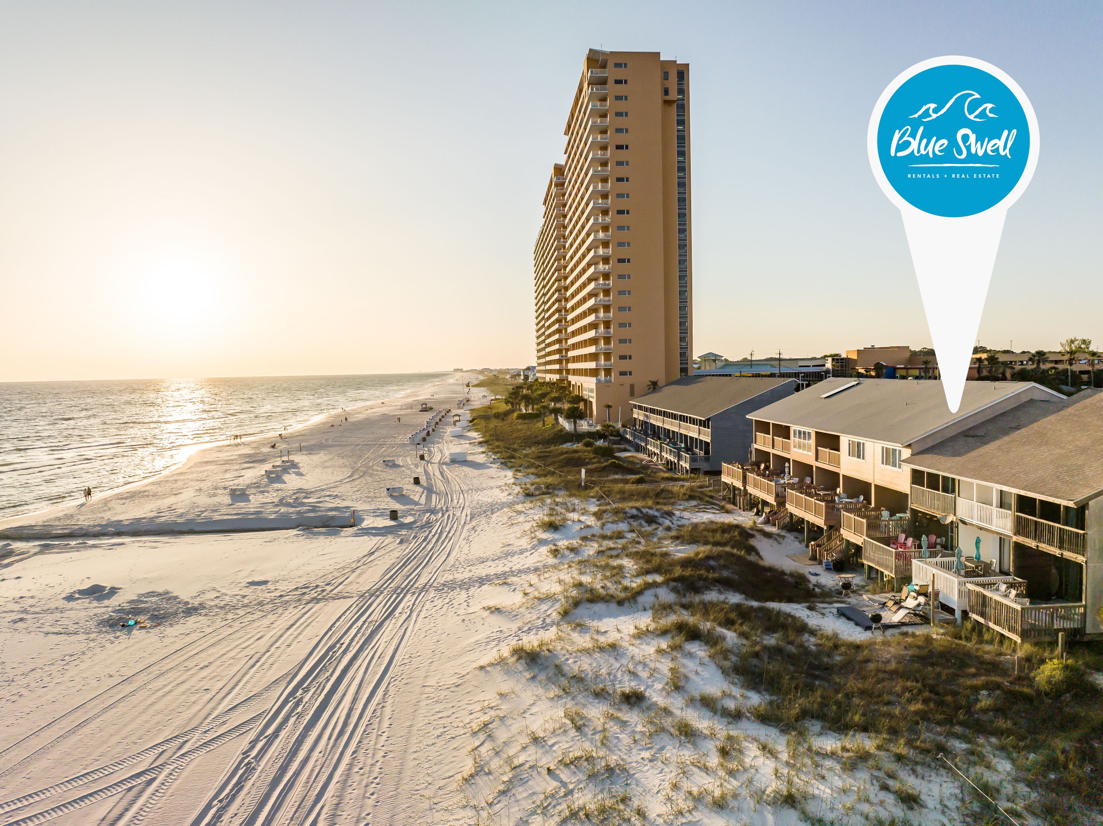 A beachfront hotel with a high-rise building adjacent to the beach, featuring outdoor seating areas and a view of the ocean.