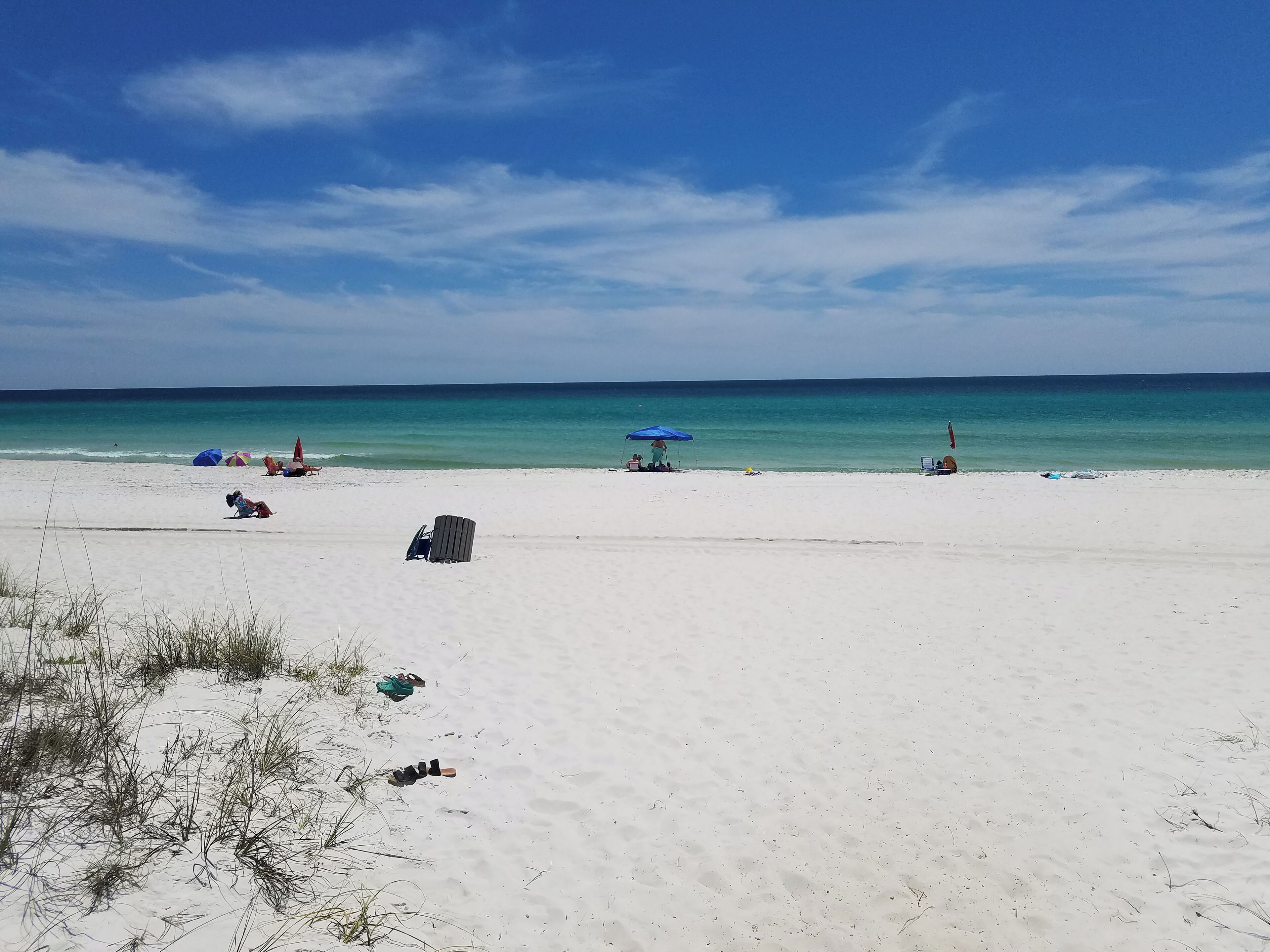 Een breed zandstrand met enkele parasols en ligbedden, een heldere lucht en rustig zeewater.