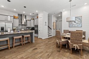 Eine moderne Küche mit einer zentralen Kochinsel, Barhocker und einem Essbereich mit Korbstühlen.